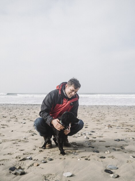 Homme jouant avec un mignon chien épagneul noir sur la plage pendant la journée