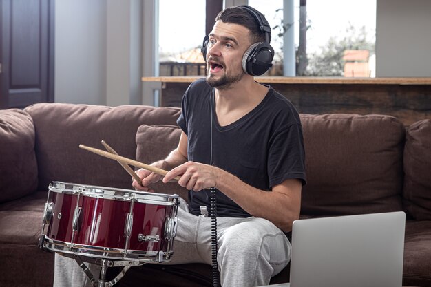 Un homme joue du tambour et regarde l'écran du portable. Le concept de cours de musique en ligne, cours de vidéoconférence.