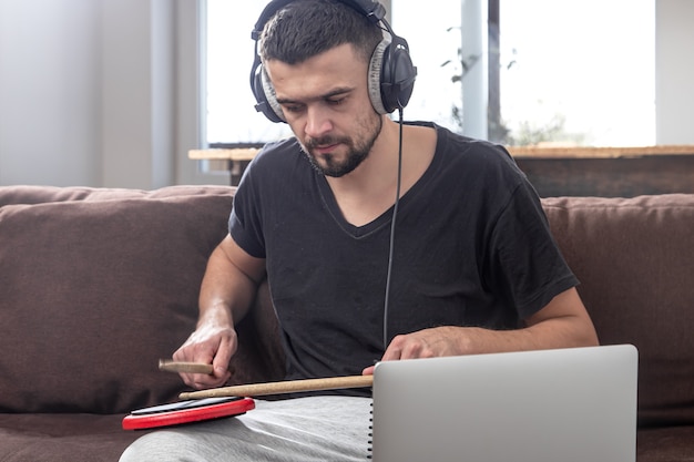 Un homme joue du tambour et regarde l'écran du portable. Le concept de cours de musique en ligne, cours de vidéoconférence.