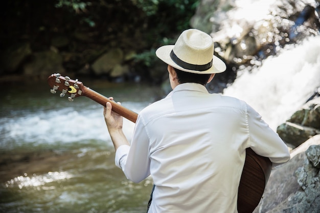 Photo gratuite homme joue de la guitare près de la cascade