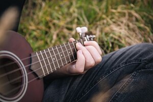 Un homme joue de la guitare ukulélé dans la nature, les doigts en gros plan serrent les cordes