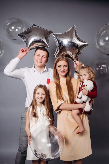 Homme joyeux et femme rousse tenant des ballons et posant avec deux adorables enfants