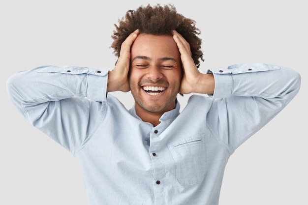 Photo gratuite un homme joyeux garde les mains sur la tête du bonheur, ferme les yeux et sourit largement de plaisir