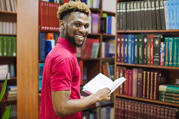 Homme joyeux noir dans la bibliothèque avec un livre