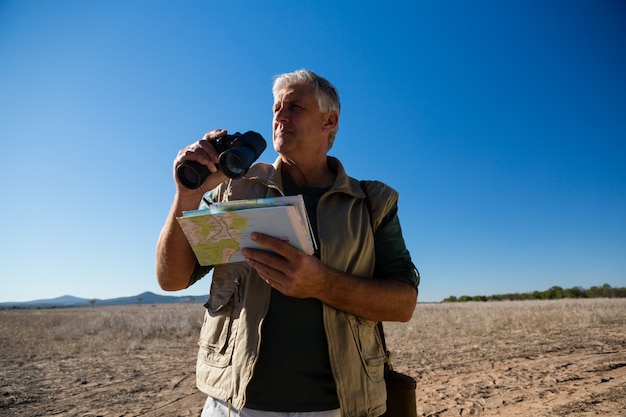 Homme avec jumelles et carte debout sur le paysage