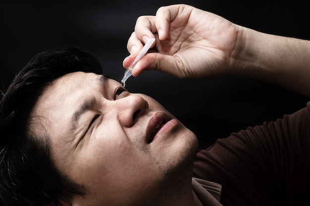 Homme laissant tomber la médecine de gouttes oculaires guérir sa douleur oculaire avec un fond noir
