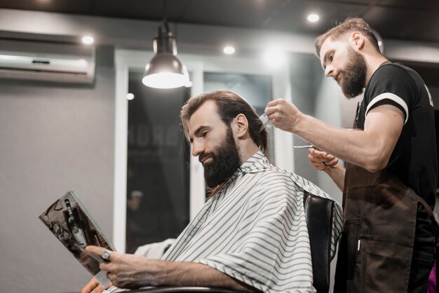 Homme lisant un magazine tout en coupant les cheveux dans un salon de coiffure