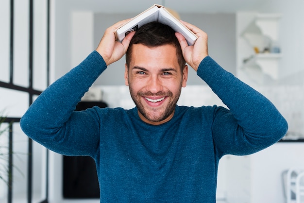 Photo gratuite homme ludique mettant un livre sur la tête