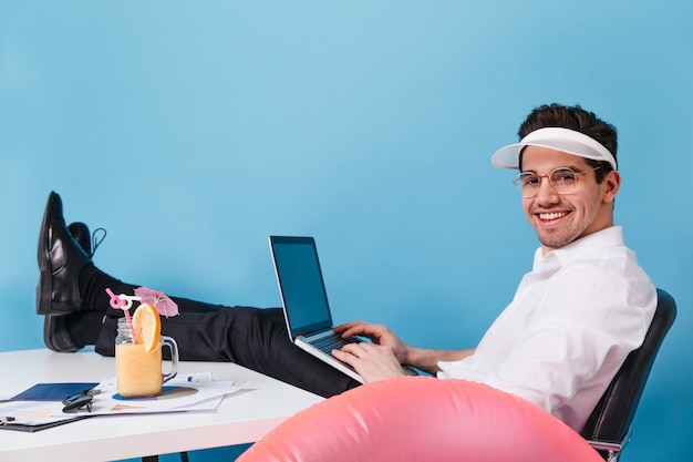 L'homme à lunettes et casquette travaille sur un espace isolé. Guy posant avec ordinateur portable, cocktail et cercle gonflable.