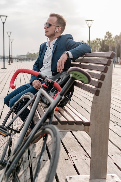Homme avec des lunettes de soleil assis sur un banc à côté de son vélo