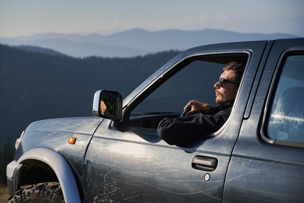 Homme avec des lunettes de soleil conduisant une voiture noire dans les montagnes