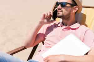 Photo gratuite homme avec des lunettes de soleil à la plage avec ordinateur portable et smartphone