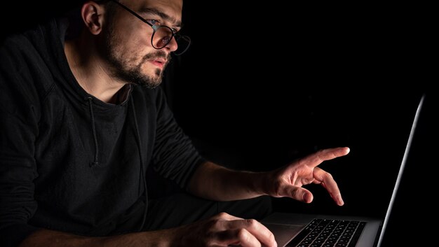 Un homme avec des lunettes travaille sur un ordinateur portable dans le noir