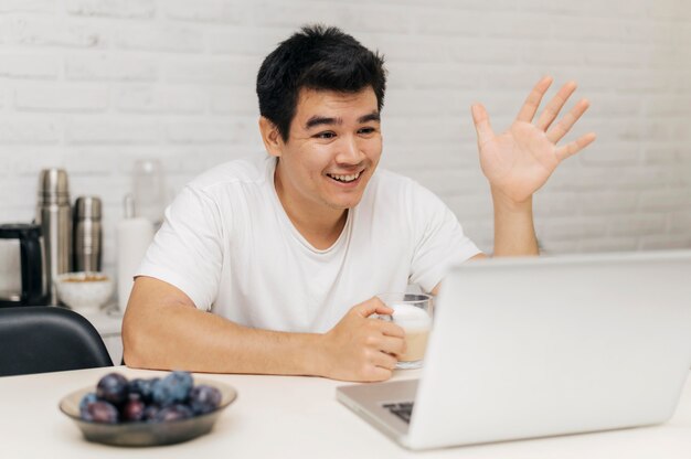 L'homme à la maison pendant la pandémie ayant un appel vidéo sur ordinateur portable et agitant