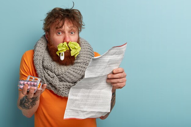 Homme malade dans des vêtements chauds avec des mouchoirs en papier dans le nez et un thermomètre