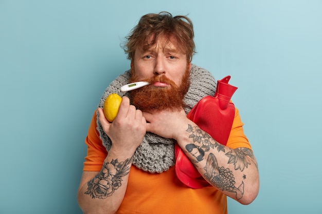 Homme malade dans des vêtements chauds avec thermomètre, détient du citron, bouillotte