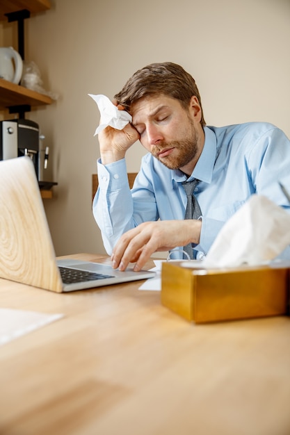 Homme malade avec mouchoir éternuements se moucher tout en travaillant au bureau