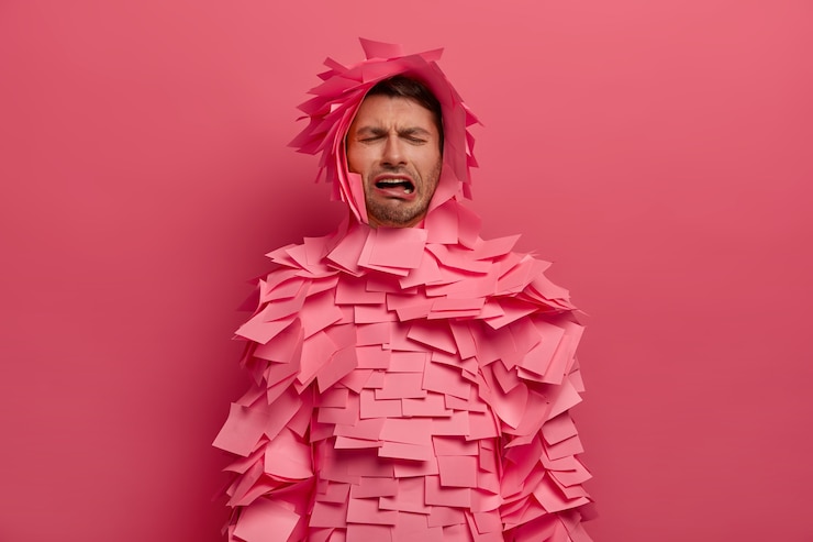 Photo gratuit un homme malheureux frustré pleure de désespoir, exprime des émotions négatives, porte des notes autocollantes autour du corps et de la tête, pose à l'intérieur contre un mur rose, a une expression misérable abattue