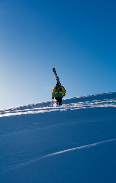 Homme avec un manteau jaune marchant dans la neige portant une planche de ski