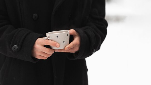 Homme en manteau noir tenant une tasse de thé