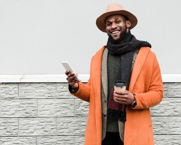 Homme en manteau orange tenant une tasse de café et un téléphone