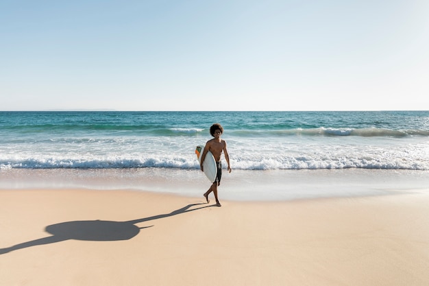 Homme marchant sur la plage avec planche de surf