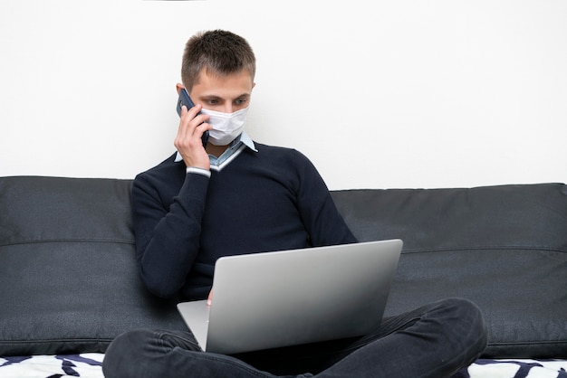 Homme avec masque médical à l'aide d'un ordinateur portable et d'un smartphone