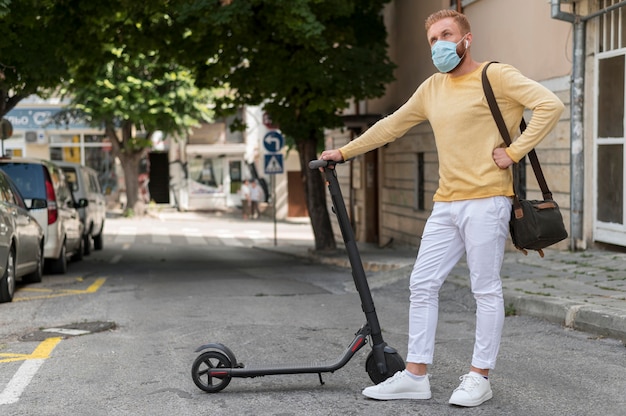 Homme avec masque médical tenant son scooter