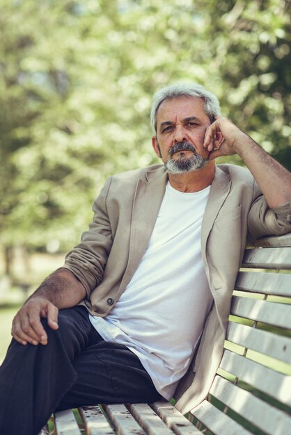 Un homme mature pensif assis sur un banc dans un parc urbain.