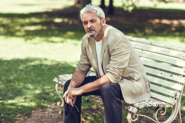 Un homme mature pensif assis sur un banc dans un parc urbain.