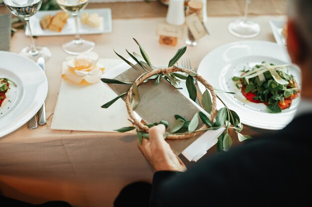 Homme méconnaissable assis à une table à manger et tenant une invitation de mariage dans la salle de réception