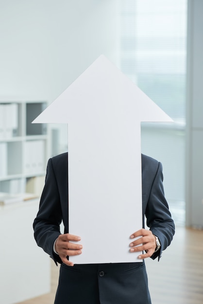 Photo gratuite homme méconnaissable en costume debout dans le bureau et tenant une grande flèche blanche pointant vers le haut