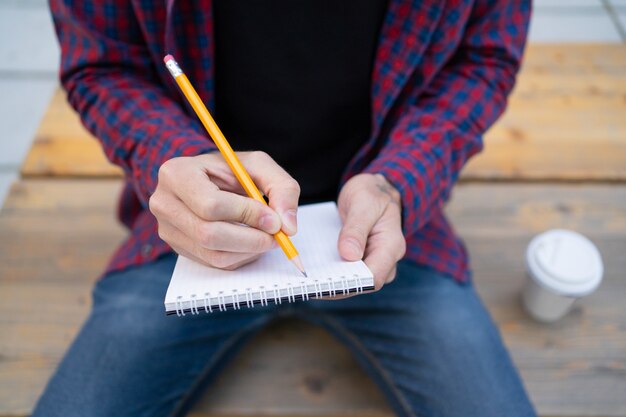 Homme méconnaissable écrit dans un cahier avec un crayon