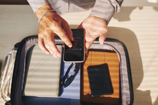 Homme méconnaissable emballant la valise et utilisant un smartphone