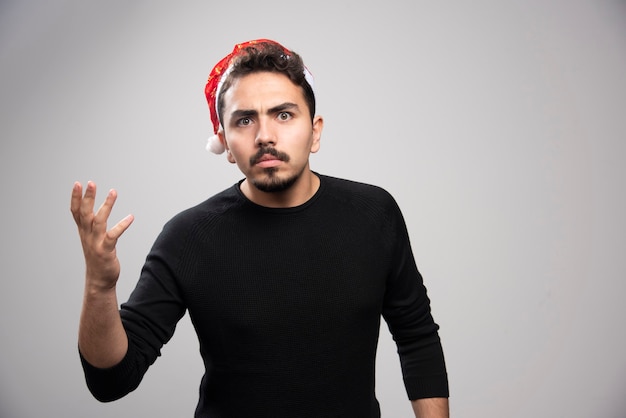 Homme mécontent portant chapeau rouge du père Noël sur un mur gris.