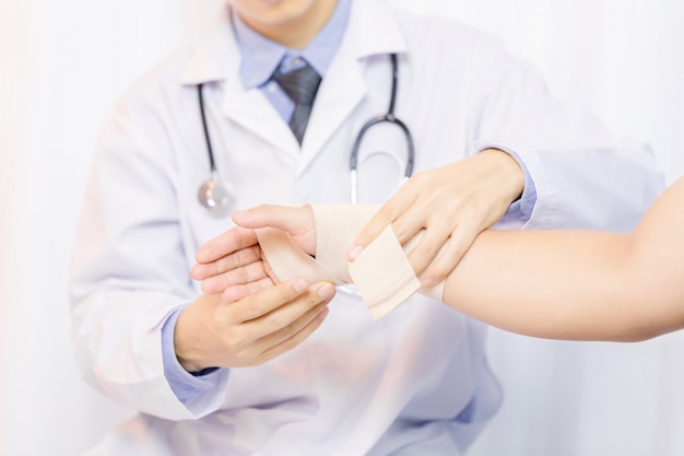 Photo gratuite homme médecin mettant la gaze sur la main du jeune homme en clinique, gros plan. premiers secours