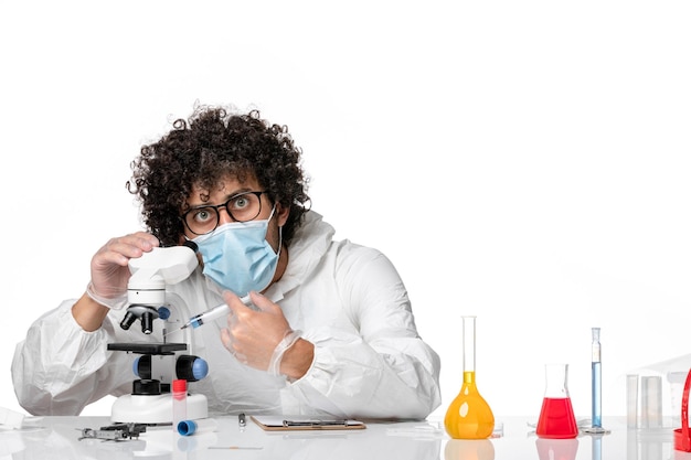 homme médecin en tenue de protection et masque travaillant avec microscope sur blanc