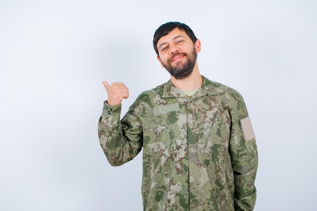 L'homme militaire heureux montre en arrière avec des pouces sur le fond blanc