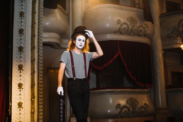 Homme mime debout sur scène avec un parapluie et portant un chapeau noir