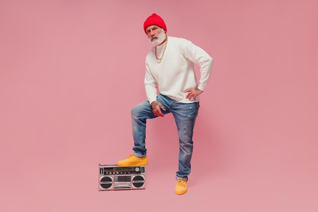 Homme de mode au chapeau rouge et chandail blanc posant avec tourne-disque Mec moderne aux cheveux gris en casquette orange avec des chaînes en or regardant dans la caméra