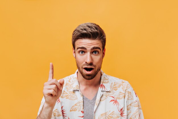 Homme moderne aux yeux bleus avec une coiffure cool et une barbe au gingembre dans des vêtements d'été à la mode imprimés ayant une idée et regardant dans la caméra