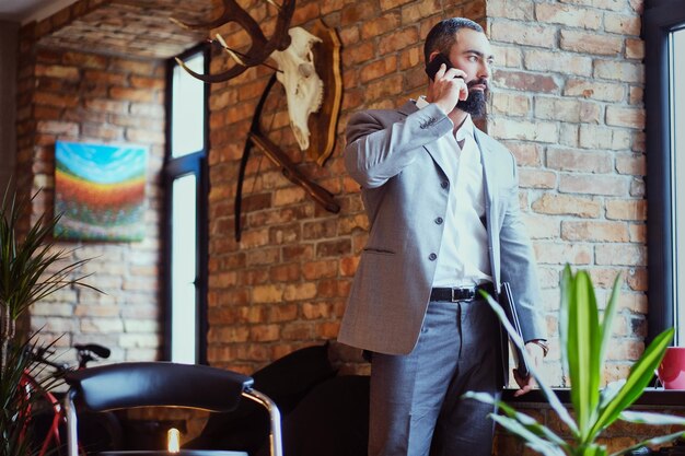 Homme moderne barbu utilisant un smartphone dans une pièce avec intérieur loft.