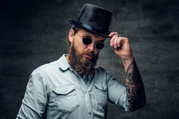 Homme moderne brutal en lunettes de soleil rétro et chapeau pose au studio photo.