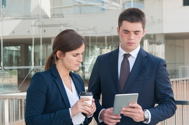 Homme montrant des données sur tablette, femme à la recherche, tenant un café