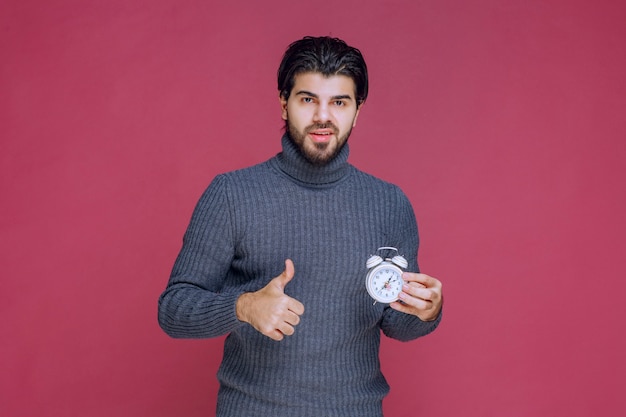 Homme montrant un réveil blanc et pointant vers une meilleure offre.