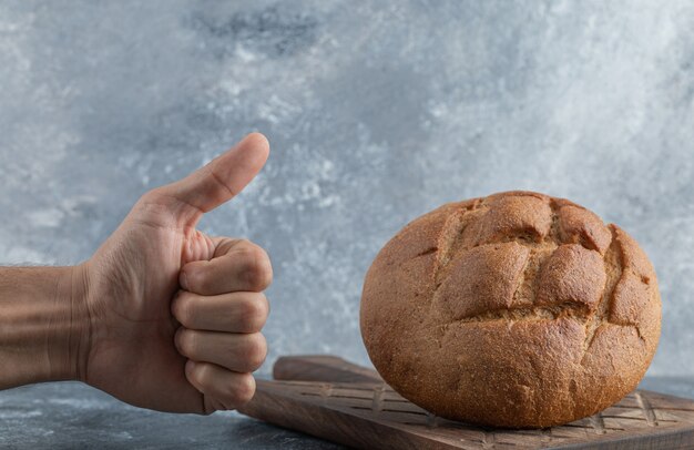 L'homme montre le pouce vers le haut pour une miche de pain de seigle. Photo de haute qualité