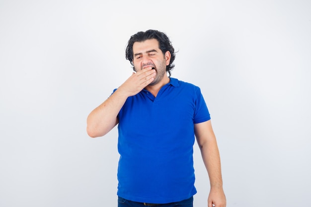 Homme mûr bâillant en t-shirt bleu et à la recherche de sommeil. vue de face.