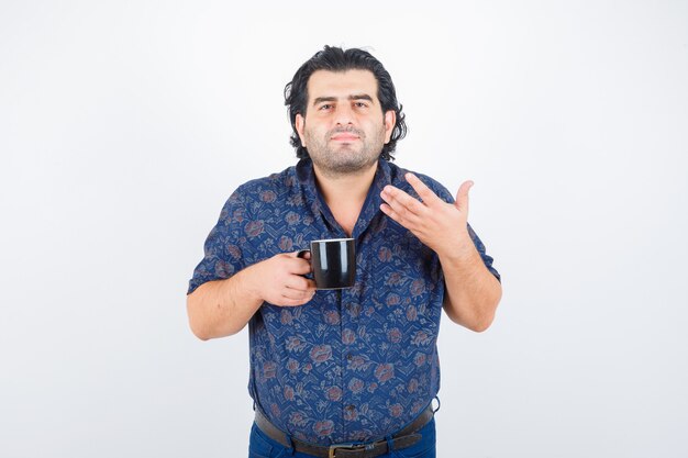 Homme mûr en chemise tenant la tasse tout en sentant le thé et à la ravie, vue de face.