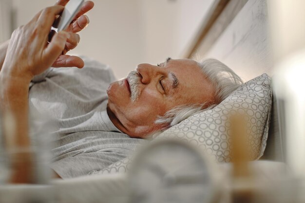 Homme mûr envoyant des SMS sur un téléphone intelligent en position couchée dans son lit