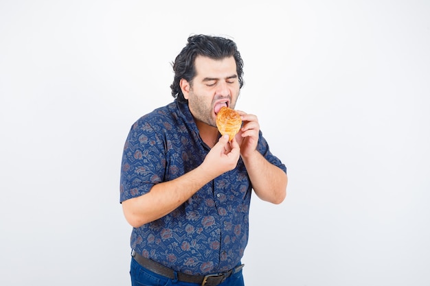 Homme mûr mangeant des produits de pâtisserie en chemise et à la faim, vue de face.